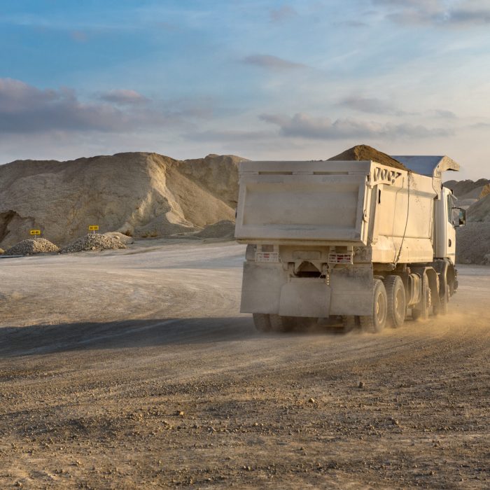 a white truck on a road in a quarry, dust illuminated by the setting sun