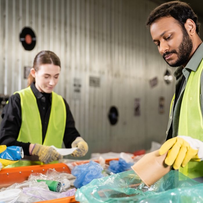Bearded indian worker in safety vest and protective gloves putting paper cup in plastic bag while