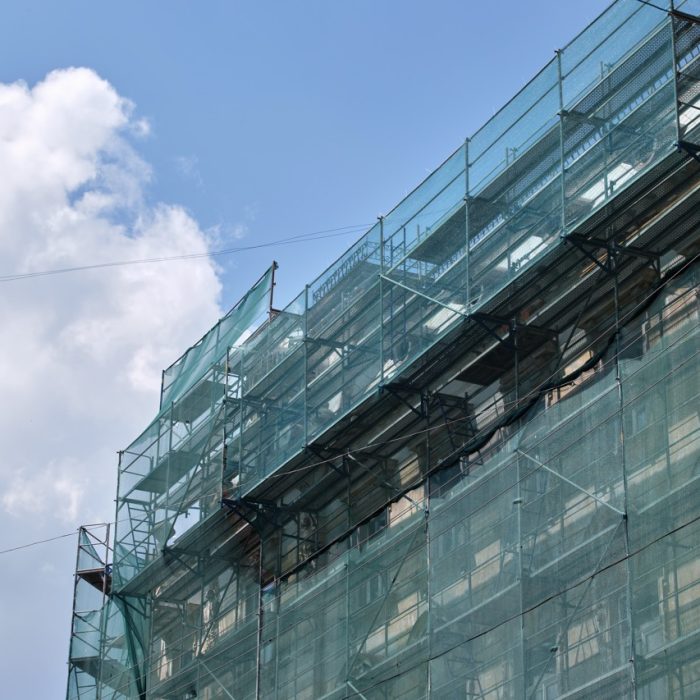 Building facade under renovation works with construction scaffolding frame covered with protective net for workers safety .