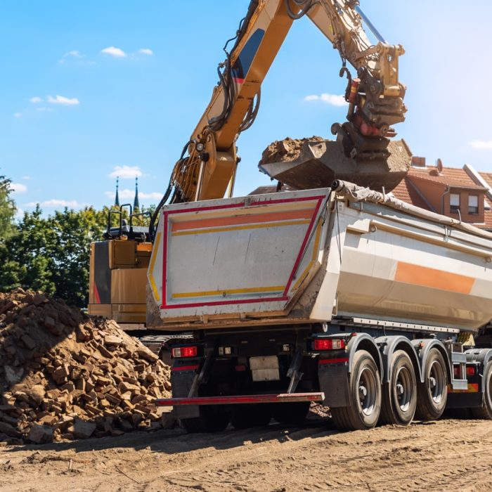 Heavy excavatore machine uploading waste and debris rubble into dump truck at construction site. Building dismantling and construction waste disposal service. Construction site industrial background.