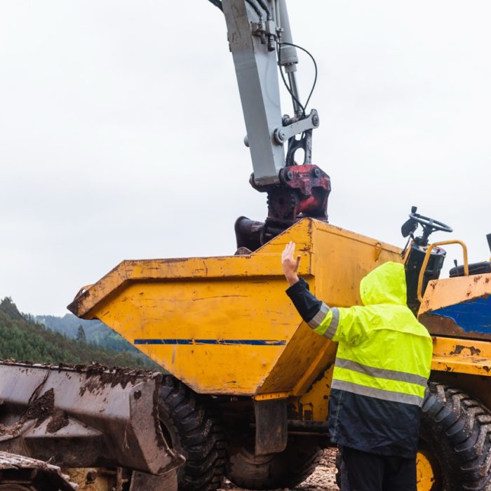 man working on the construction of a mountain road gives orders and signals to his co-workers. excavator shovel emptying cargo on a cargo vehicle in the mountains